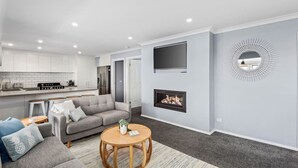 A modern living room with a grey sofa, a round wooden coffee table, and a fireplace. - Hood Road Beach House- Hamptons inspired sleeps 9 (Indented Head)