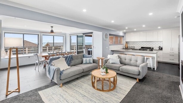 A modern living room with a grey sofa, a wooden coffee table, and a dining area with a white table and chairs. - Hood Road Beach House- Hamptons inspired sleeps 9 (Indented Head)