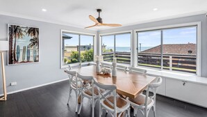 A dining area with a large wooden table, white chairs, and a ceiling fan. - Hood Road Beach House- Hamptons inspired sleeps 9 (Indented Head)