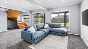 A modern living room with a sectional sofa, a staircase, and large windows. - Hood Road Beach House- Hamptons inspired sleeps 9 (Indented Head)