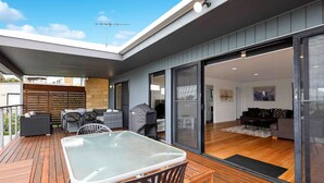 A modern outdoor patio with a glass table and chairs, a barbecue grill, and a wooden deck. - Ocean Escape- 5 Bedroom, 3 bath- Sleeps 11, beach (Ocean Grove)