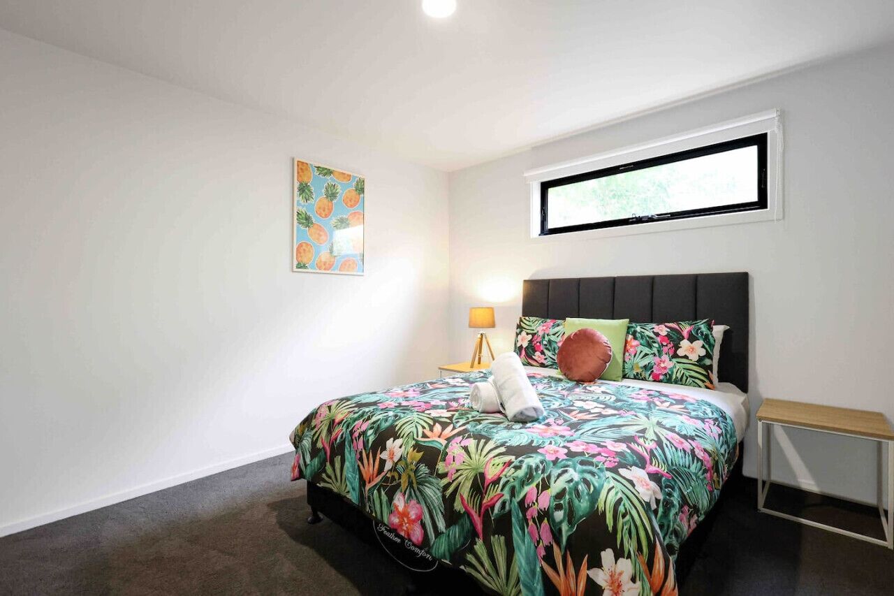 A bedroom with a bed, a nightstand, a lamp, a window, and a wall art piece.