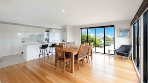 A modern kitchen with white cabinets, a wooden dining table with six chairs, and a large window with a view of greenery. - Ocean Escape- 5 Bedroom, 3 bath- Sleeps 11, beach (Ocean Grove)
