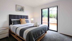 A bedroom with a bed, a nightstand, a bedside lamp, a framed picture on the wall, and a sliding glass door leading to an outdoor area. - Ocean Escape- 5 Bedroom, 3 bath- Sleeps 11, beach (Ocean Grove)