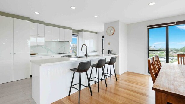 A modern kitchen with white cabinets, a central island with bar stools, and a dining area with a wooden table and chairs. - Ocean Escape- 5 Bedroom, 3 bath- Sleeps 11, beach (Ocean Grove)