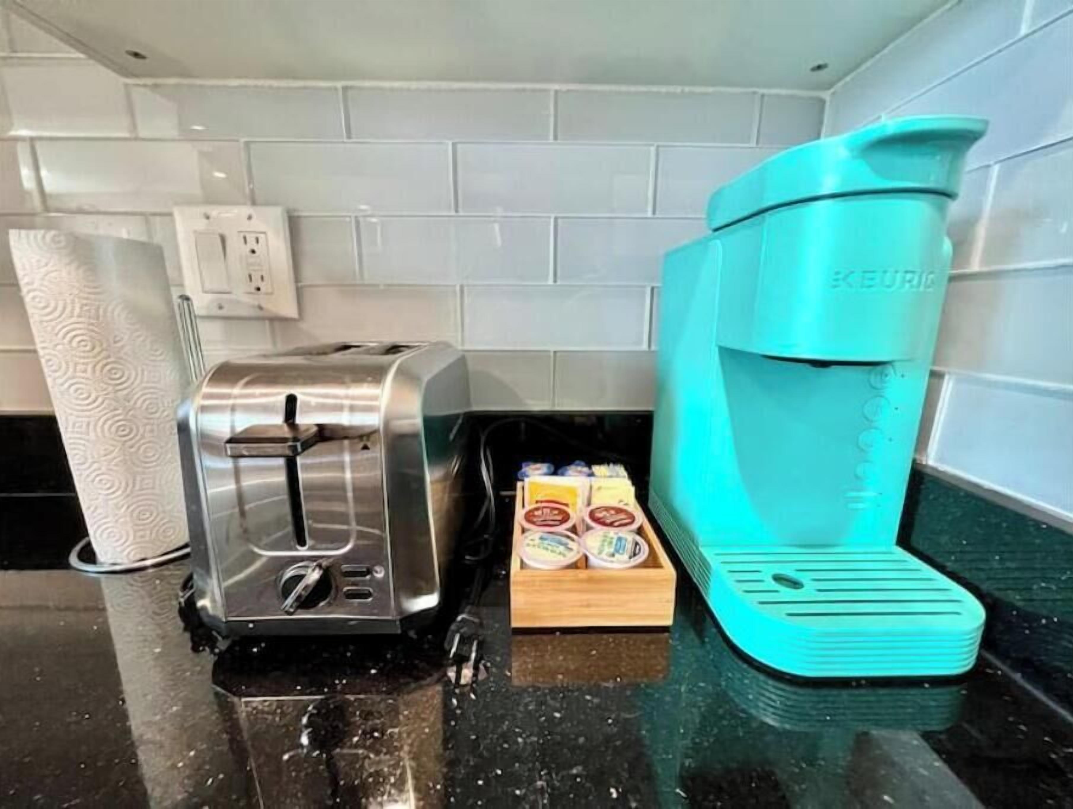 A kitchen with a toaster, a teal coffee maker, and a box of coffee pods on the counter.
