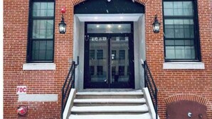 A brick building with a double door entrance, two windows on either side, and a staircase leading up to the door.