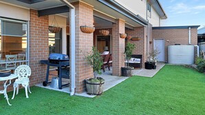 A modern house with a covered patio, a barbecue grill, and a well-maintained lawn.