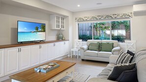 A living room with a television, white cabinets, a sofa, and a window with a view of greenery.