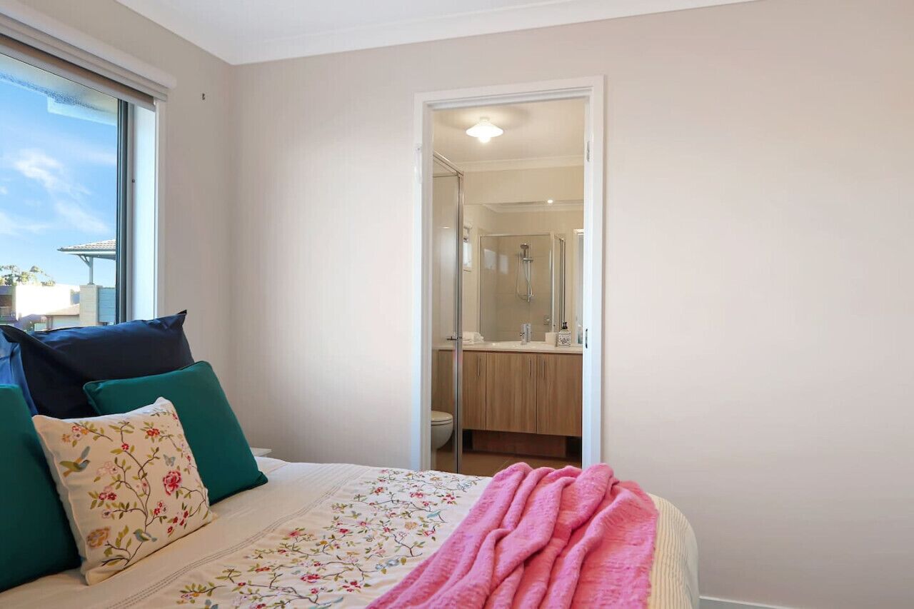 A bedroom with a bed, pillows, a blanket, and a view of a bathroom through an open door.