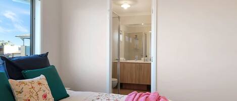 A bedroom with a bed, pillows, a blanket, and a view of a bathroom through an open door.