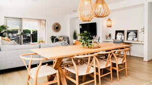 A modern living room with a wooden dining table, light grey sofa, and wicker pendant lights. - Hamptons Haven; Luxe 4 bedroom, 2 bathroom, WIFI (Armstrong Creek)