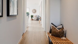 A hallway with a wooden bench, framed artwork on the walls, and a view into a living area with a sofa and a round mirror. - Hamptons Haven; Luxe 4 bedroom, 2 bathroom, WIFI (Armstrong Creek)