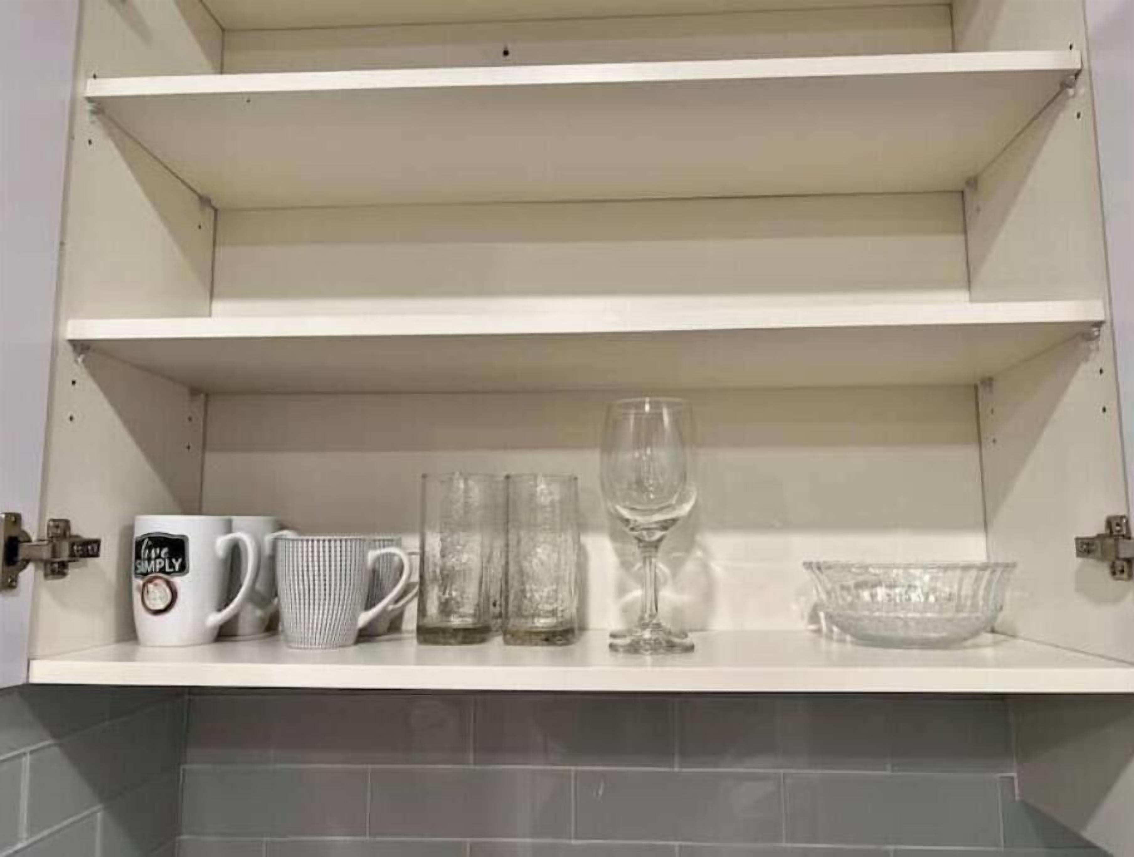 Un meuble de cuisine contenant trois tasses blanches, deux verres transparents et un verre à vin sur l’étagère supérieure.
