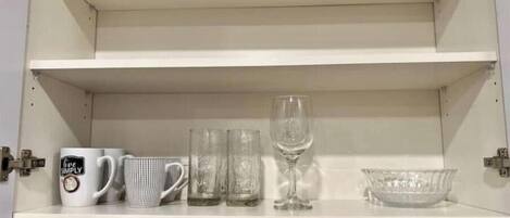 Un meuble de cuisine contenant trois tasses blanches, deux verres transparents et un verre à vin sur l’étagère supérieure.