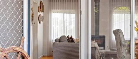 Ein gemütliches Wohnzimmer mit Holzboden, einem grauen Sofa, einem Korbhundebett mit zwei schwarzen Hunden, einem großen Fenster und einem dekorativen Krebs an der Wand.