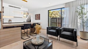A modern living room with a dining area, a black sofa, a coffee table with a vase, and a large window with curtains.