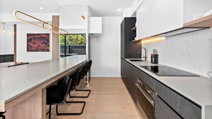 A modern kitchen with a long island, black bar stools, and a view of greenery outside.