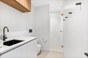 Ein modernes Badezimmer mit Waschbecken, Toilette und Duschbereich, alles in Weiß.