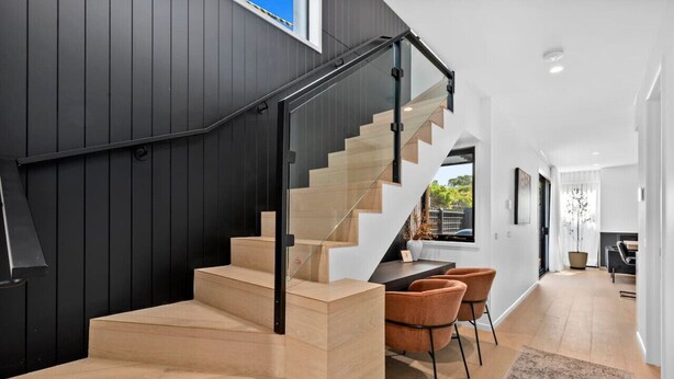 A modern staircase with wooden steps and a glass railing, leading to a dining area with two chairs and a table.
