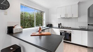 A modern kitchen with white cabinets, a black countertop, a built-in oven, and a window providing a view of greenery.