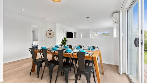 A dining area with a wooden table set for four, black chairs, and a large window with a view of the outdoors.