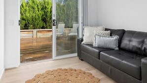A modern living room with a sliding glass door leading to an outdoor patio, a dark leather sofa, and a woven rug.