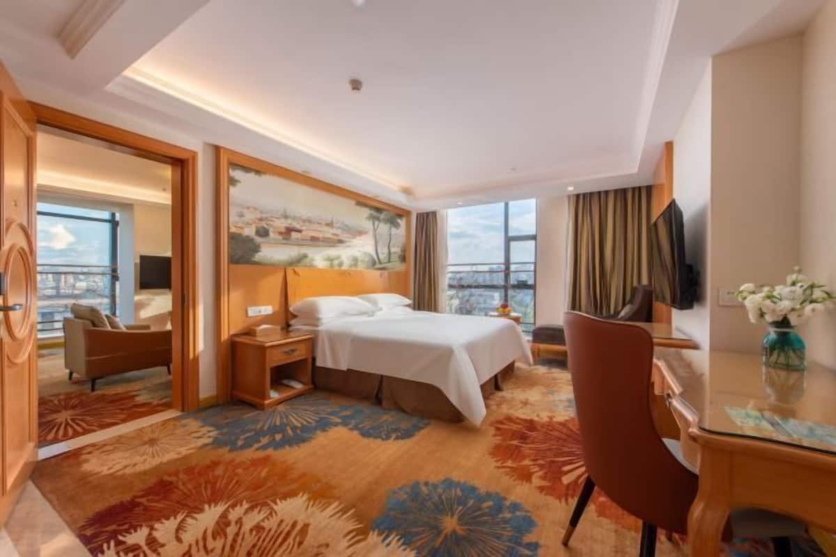 A hotel room with a bed, a desk, a chair, a TV, and a large window with a view.