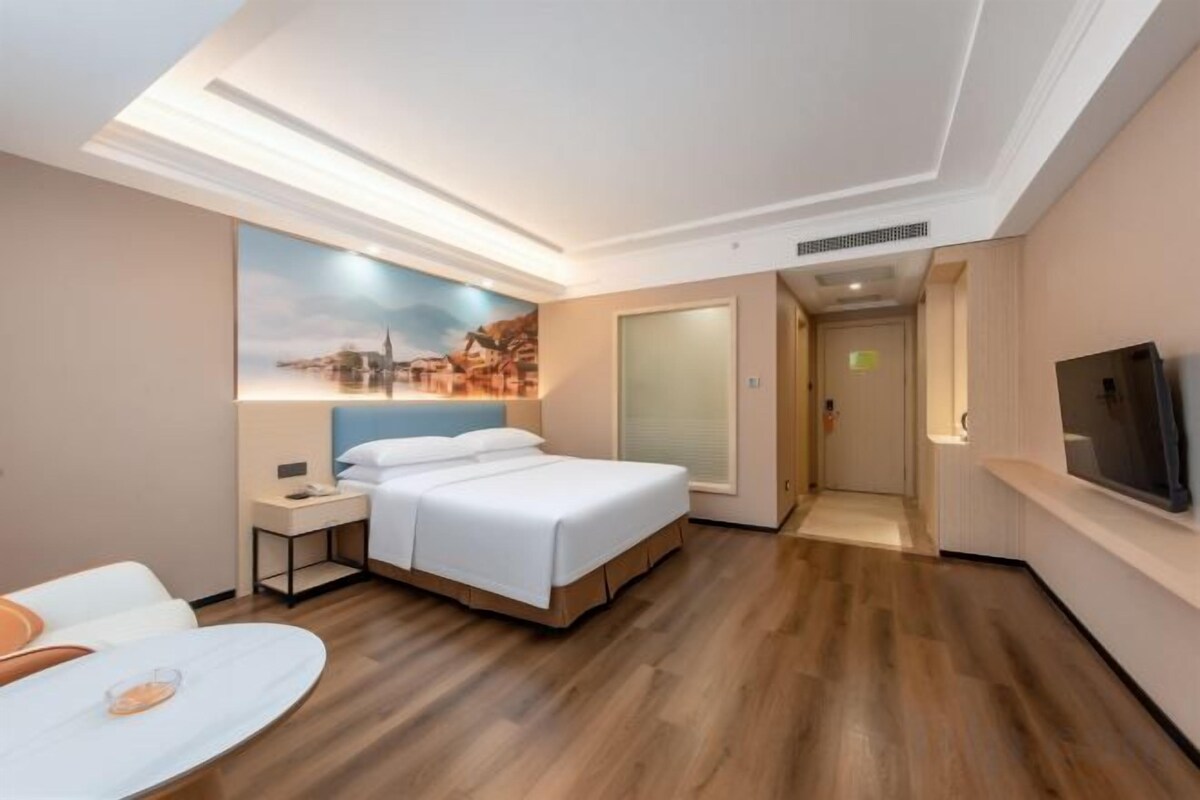 A hotel room with a bed, a desk, a chair, a TV, and a painting on the wall.