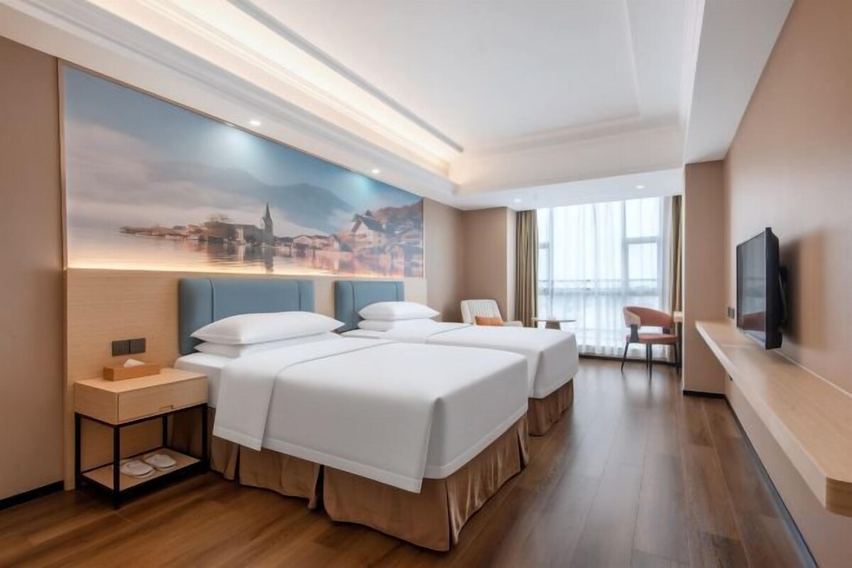 A hotel room with two beds, a nightstand, a TV, and a large window.