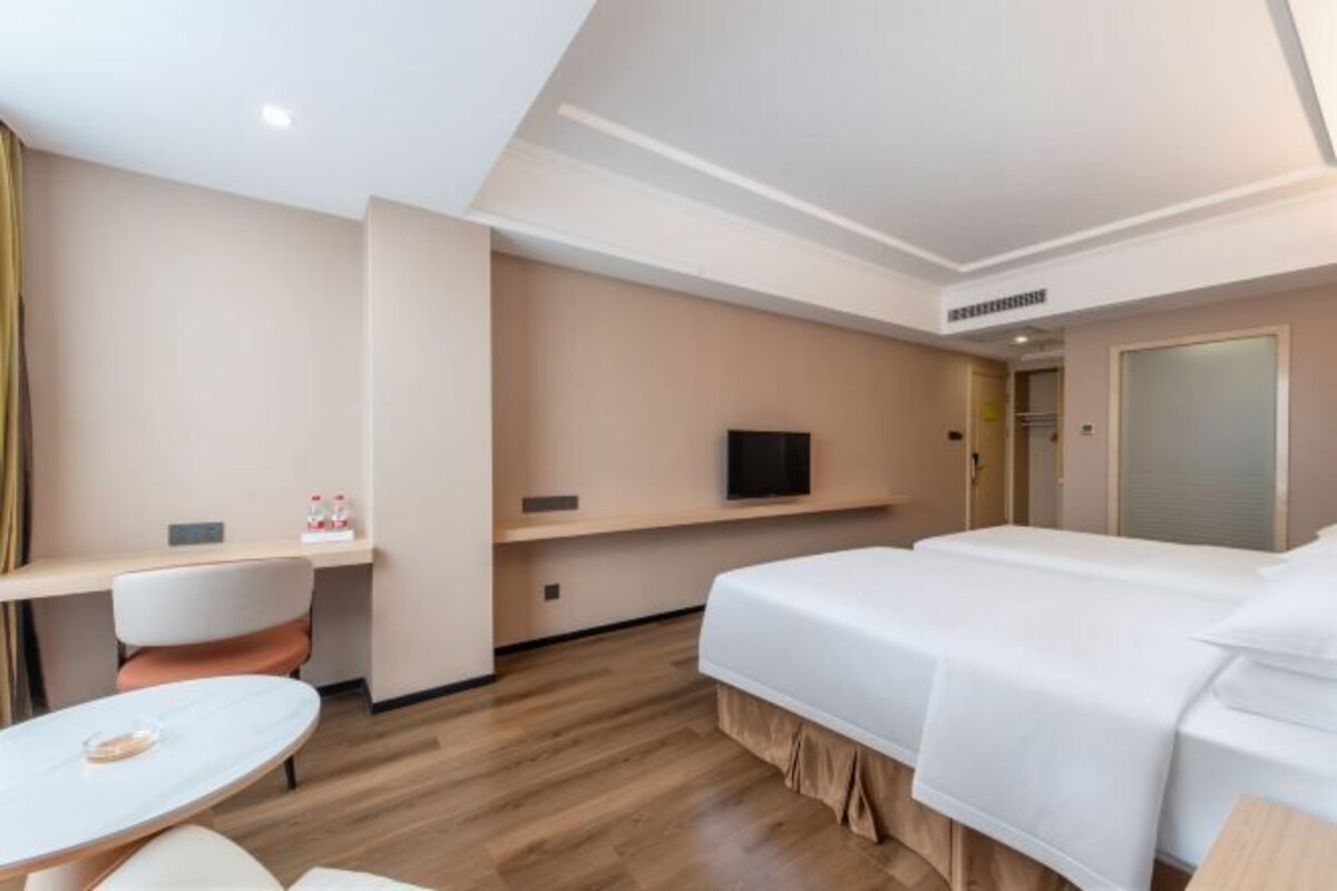A hotel room with a bed, a desk, a chair, a TV, and a small table.