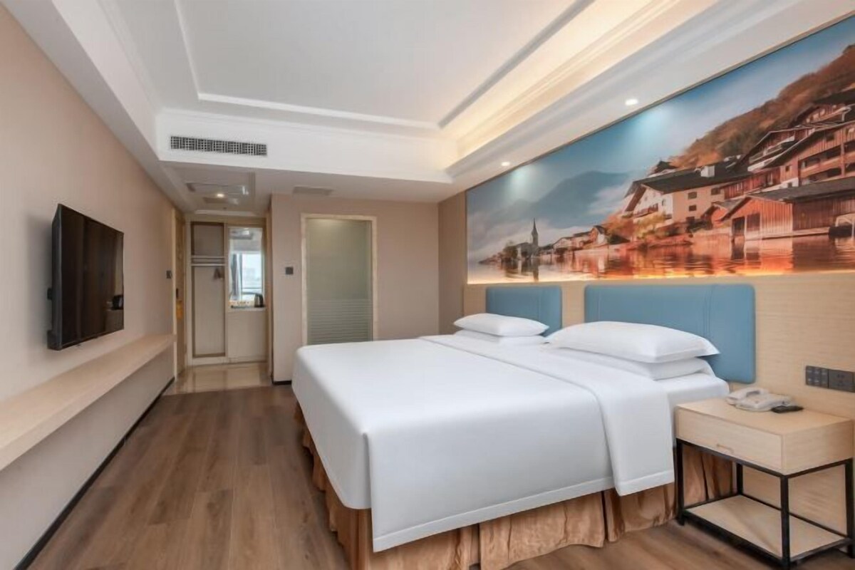 A hotel room with a bed, a desk, a flat-screen TV, and a painting on the wall.
