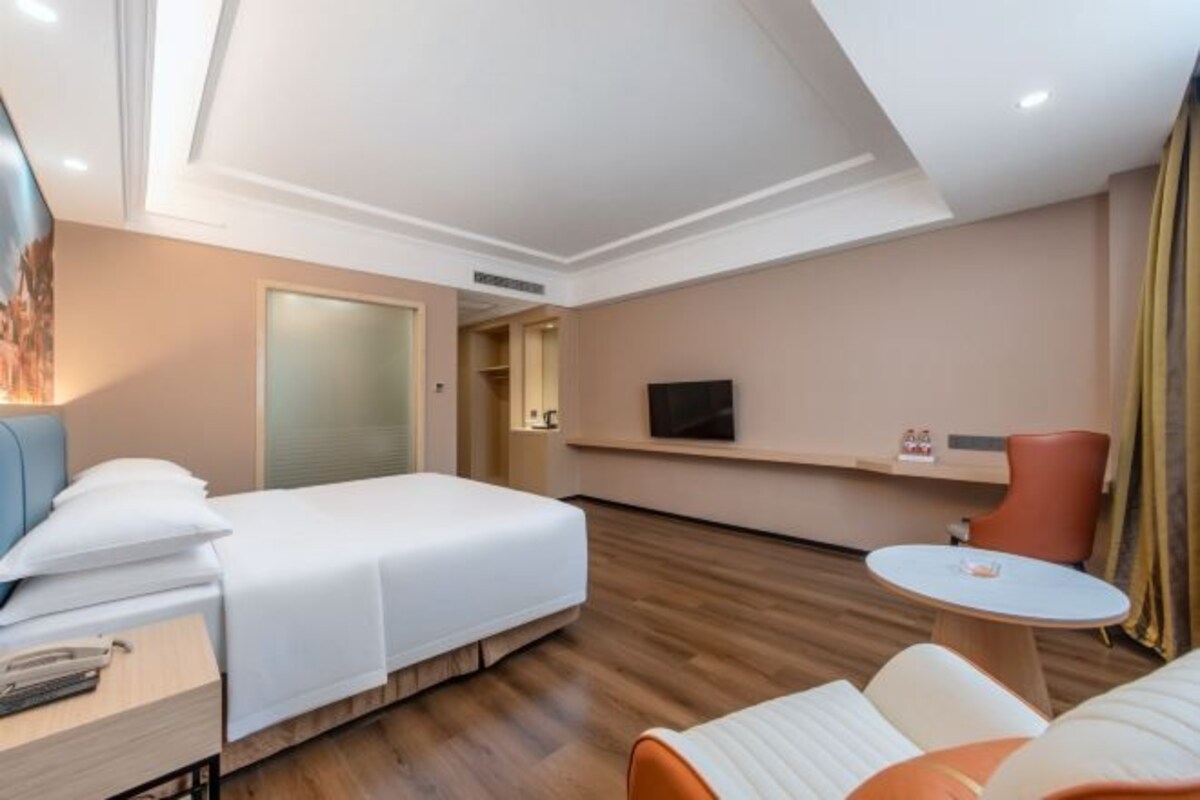 A hotel room with a bed, a desk, a chair, a television, and a small table.