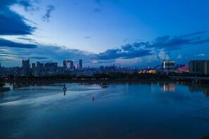 A cityscape at dusk with a calm body of water reflecting buildings. - Vienna Hotel (Guangzhou Panyu Chimelong Dashi Jiangjing Garden Branch) (Guangzhou)