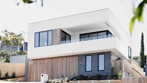 A modern two-story house with large windows, a flat roof, and a wooden fence.