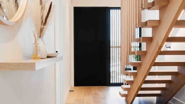 A modern interior with a wooden staircase, a black door, and a wooden floor.