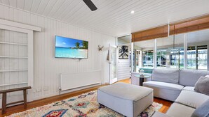 A spacious living room with a white wooden interior, a large window, a gray sofa, and a colorful rug.