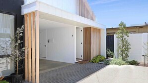 A modern building with a white exterior, a black section on the left, and a number '5' on the wall. - Beach luxury retreat- 2 bedroom, 2 bathroom, shops (Ocean Grove)