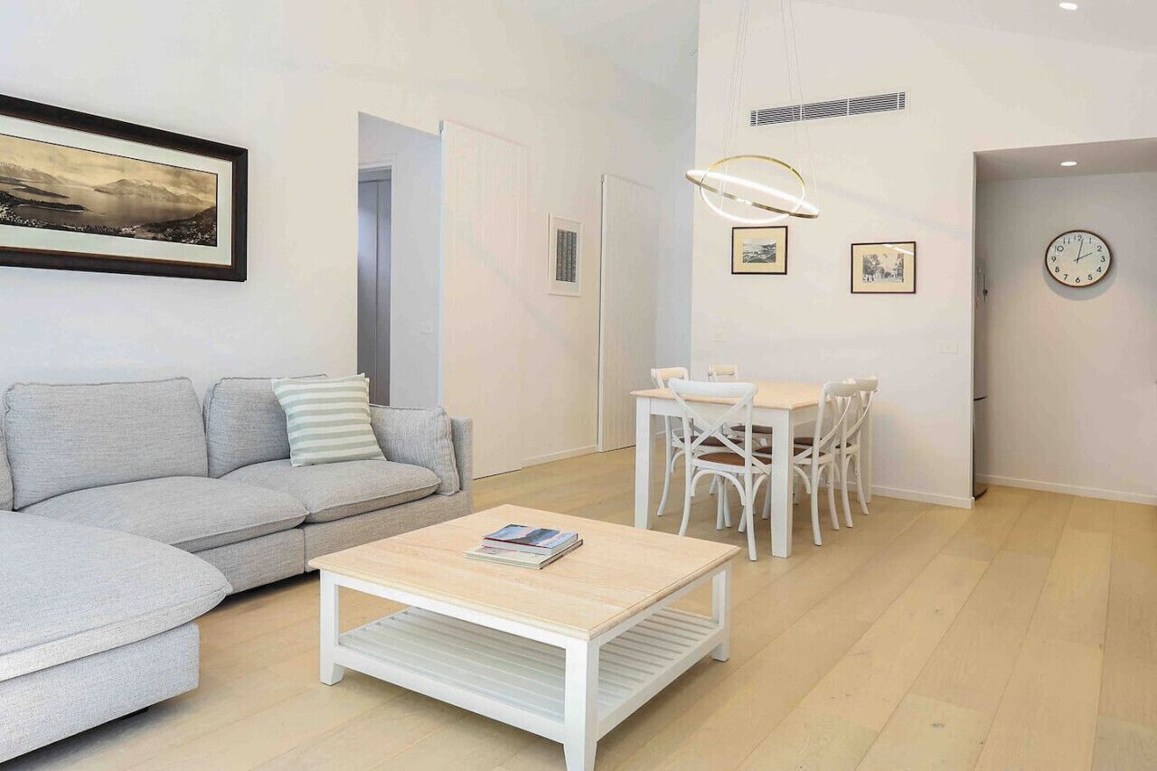 Een moderne woonkamer met een grijze bank, een witte salontafel en een eethoek met witte stoelen en een tafel.