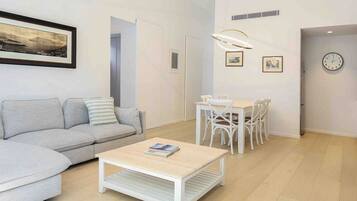 Een moderne woonkamer met een grijze bank, een witte salontafel en een eethoek met witte stoelen en een tafel.