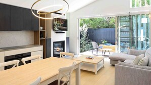 A modern kitchen with a dining area, a fireplace, and a large sliding glass door leading to an outdoor patio. - Beach luxury retreat- 2 bedroom, 2 bathroom, shops (Ocean Grove)