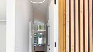 A modern interior with a wooden slat wall, a hallway leading to a living area, and a ceiling with recessed lighting. - Beach luxury retreat- 2 bedroom, 2 bathroom, shops (Ocean Grove)