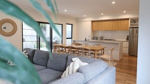 A modern kitchen with wooden cabinets, a stainless steel refrigerator, and a dining area with a wooden table and chairs. - Madeley Family Getaway- Sleeping 8, central, a/c (Ocean Grove)