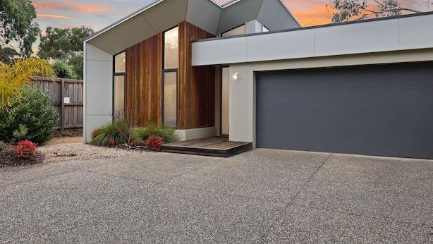 A modern two-story house with a garage, a wooden front door, and a gravel driveway. - Madeley Family Getaway- Sleeping 8, central, a/c (Ocean Grove)