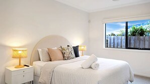 A bedroom with a bed, two bedside tables, lamps, a window with a view of greenery, and a white wall. - Madeley Family Getaway- Sleeping 8, central, a/c (Ocean Grove)