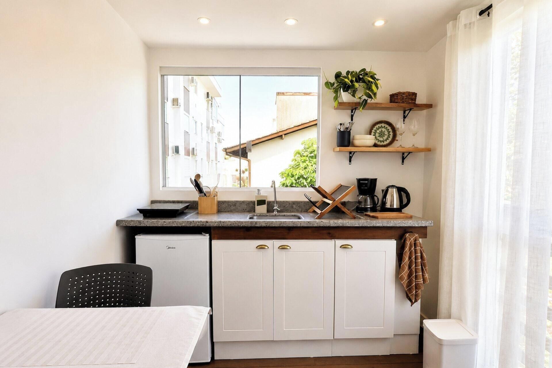 A compact kitchen with a window, a sink, a coffee maker, and a small refrigerator.