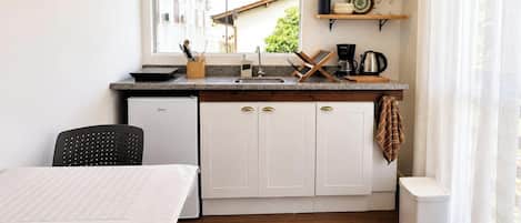 A compact kitchen with a window, a sink, a coffee maker, and a small refrigerator.