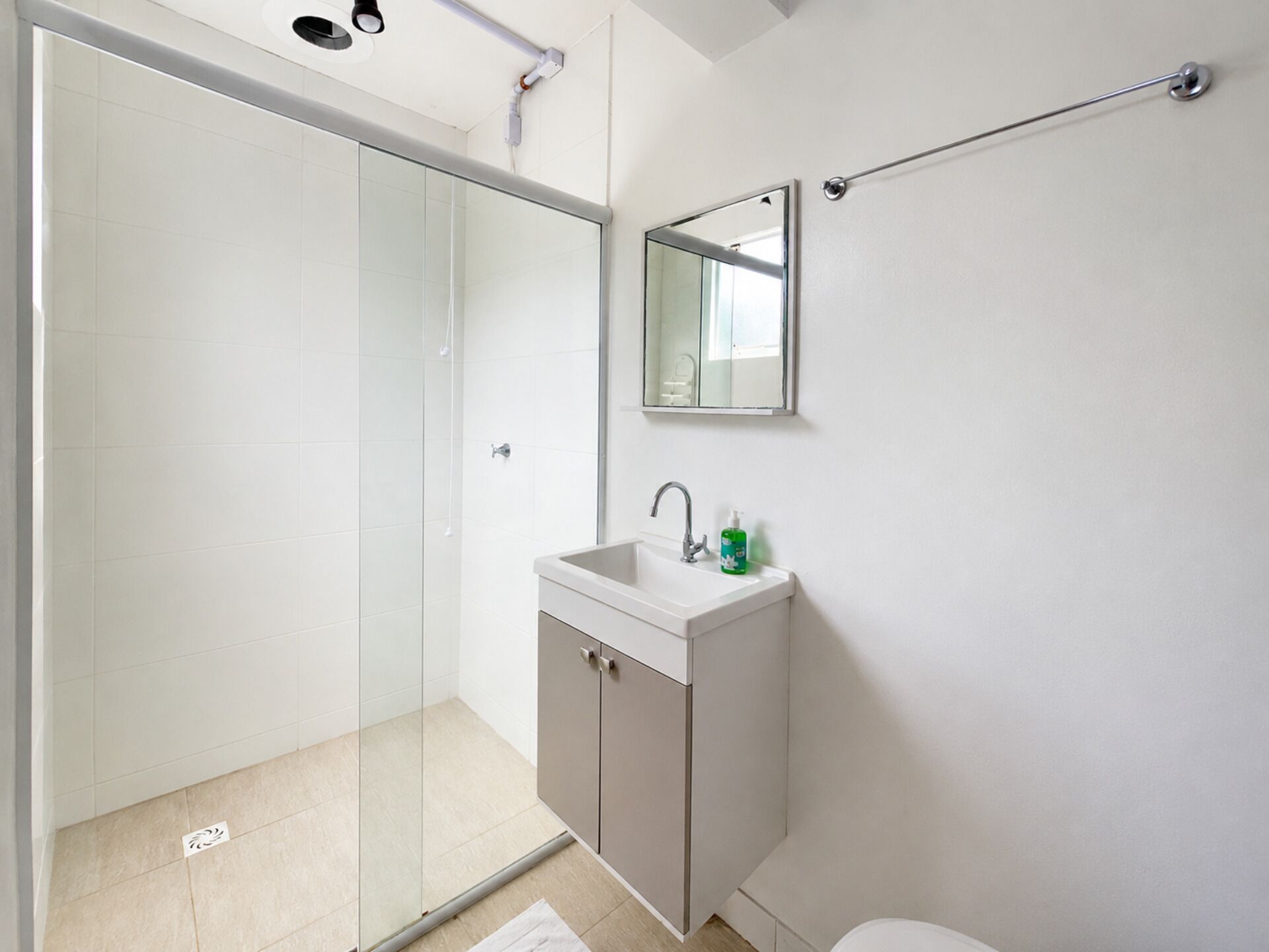 A modern bathroom with a glass shower enclosure, a white sink with a mirror above it, and a towel rack on the wall.