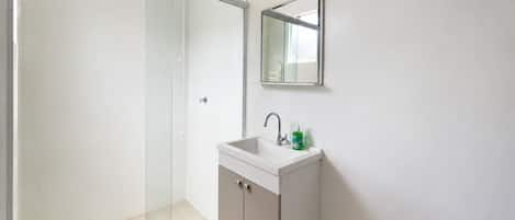 A modern bathroom with a glass shower enclosure, a white sink with a mirror above it, and a towel rack on the wall.