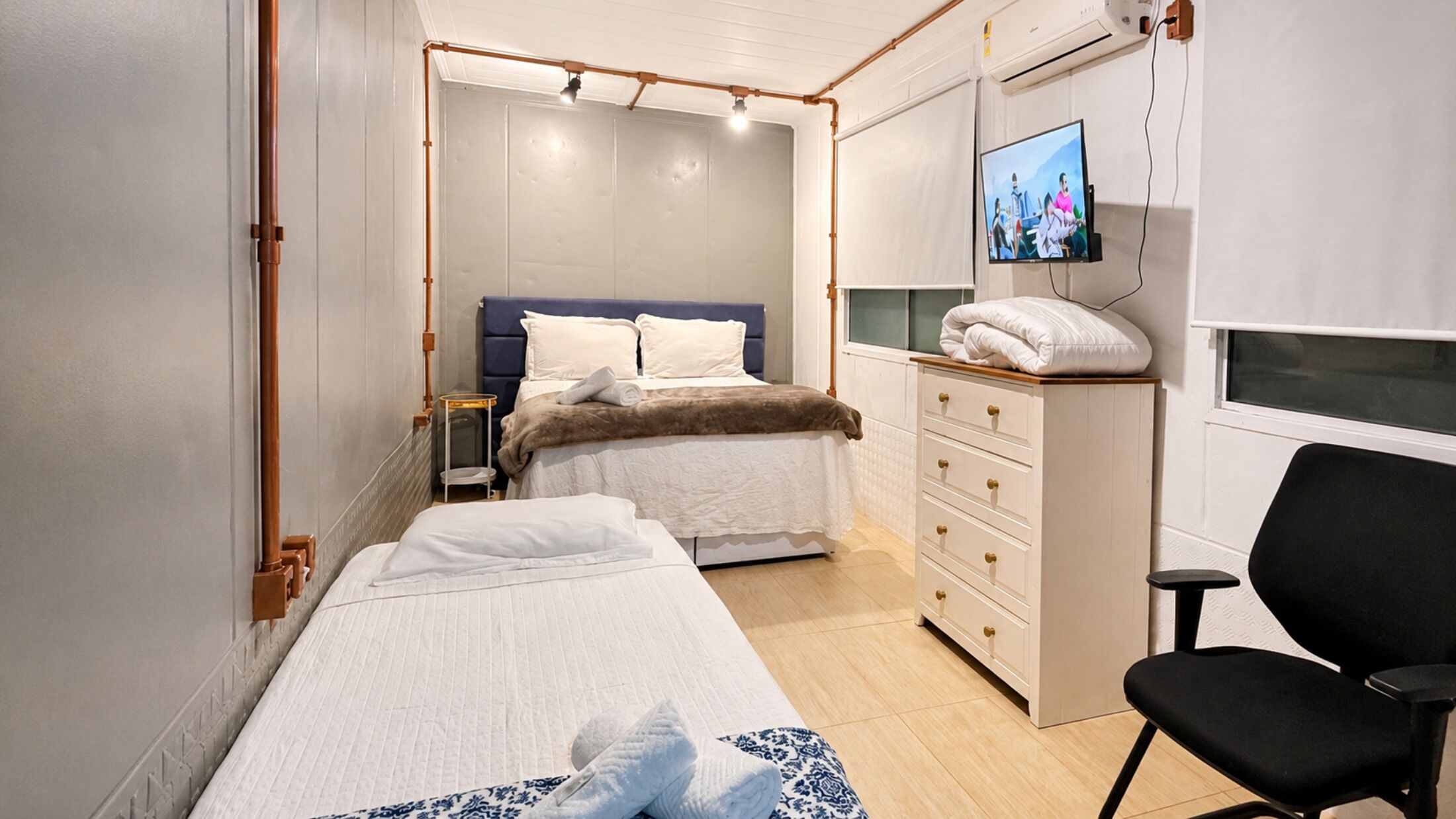 Una habitación de hotel con cama, una silla, un televisor y un aparador.